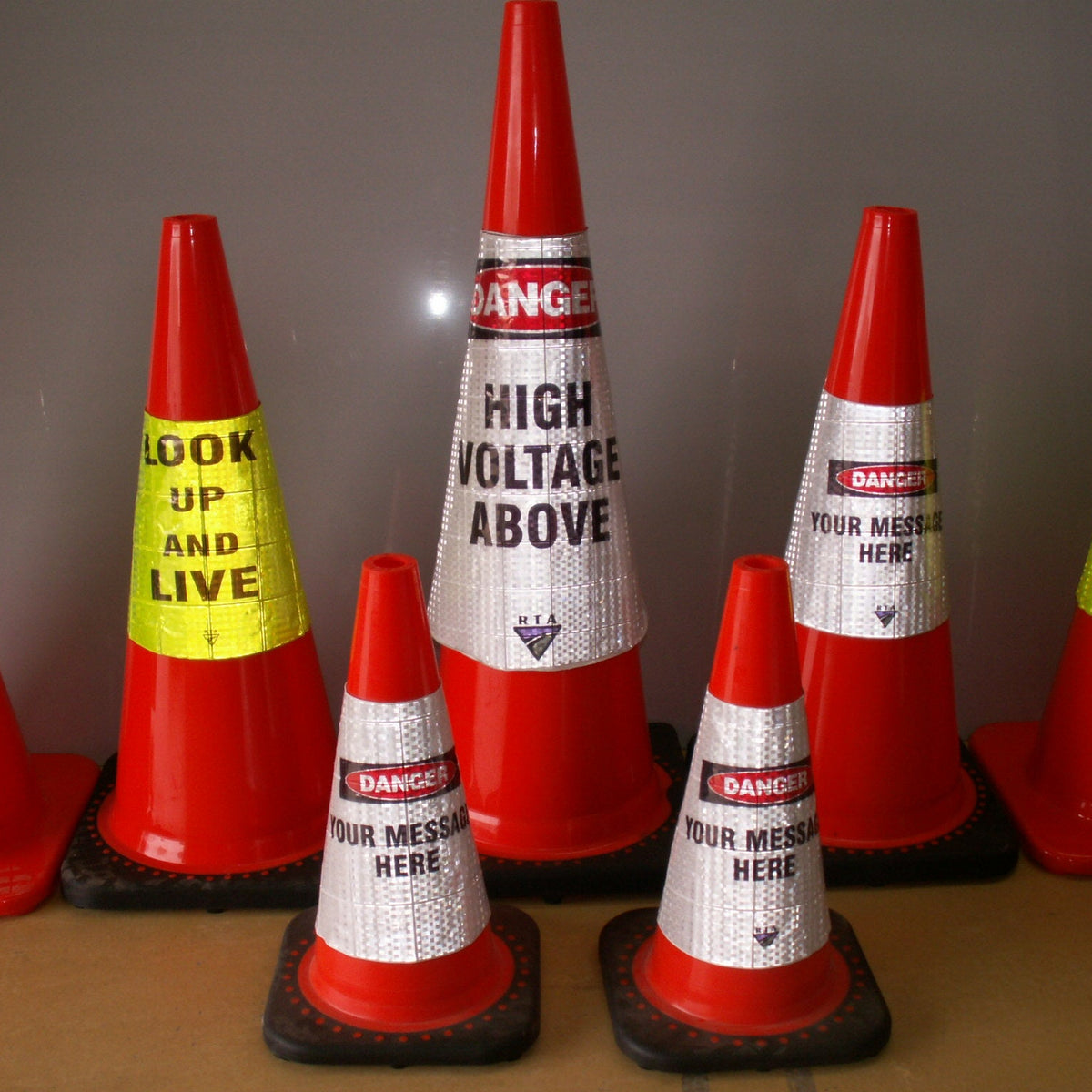 A set of red and white traffic safety cones with customizable printed warning labels, displayed on a brown surface against a gray background.