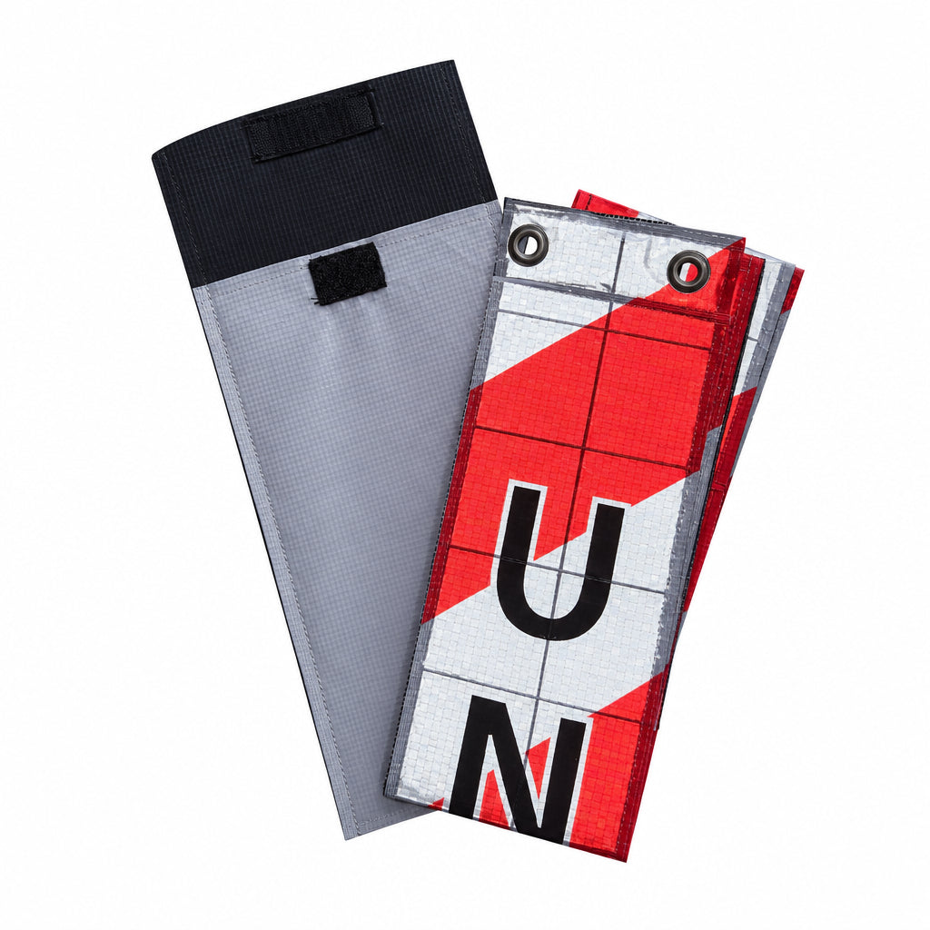 A pair of athletic running shorts in a gray and black zippered pouch, with the shorts themselves featuring a red, white, and black geometric pattern with the letters 'U' and 'N' printed on them.
