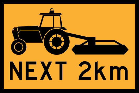 Construction sign with black tractor silhouette and 'NEXT 2km' text on a yellow background